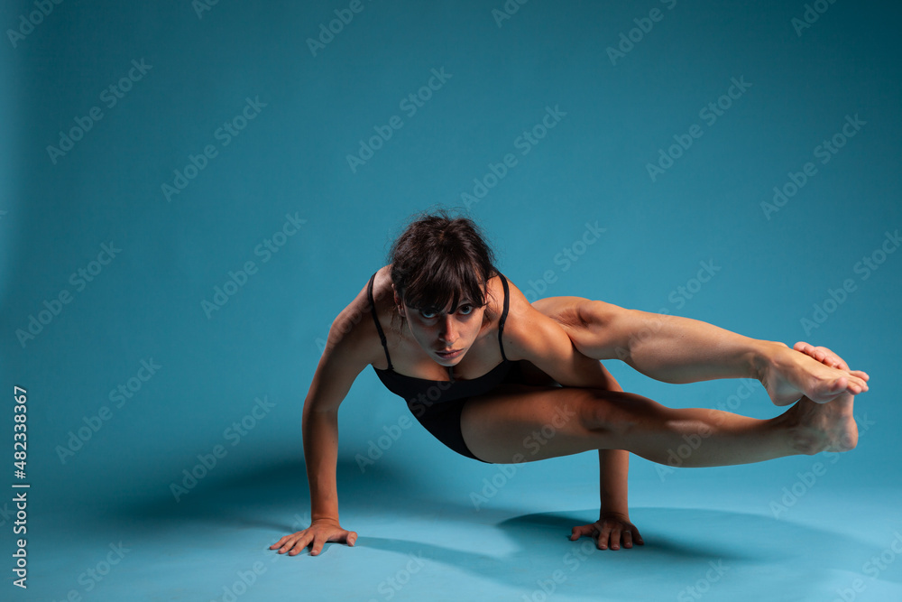 Active fit person standing in hands working at arm balance in studio with blue background. Personal trainer practicing gym exercices stretching body muscles during sport workout Active fit person standing in hands working at arm balance in studio with blue background. Personal trainer practicing gym exercices stretching body muscles during sport workout