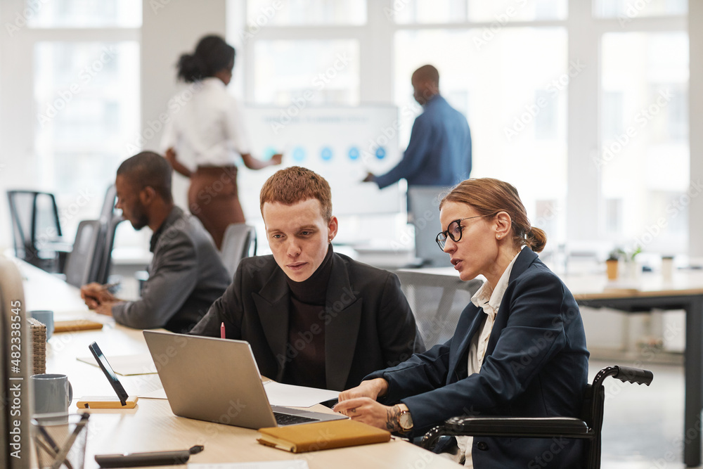 Side view portrait of young businesswoman using wheelchair while working with laptop in office, copy space Side view portrait of young businesswoman using wheelchair while working with laptop in office, copy space