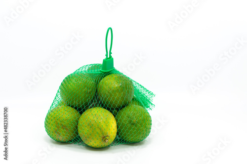 Seedless green lemons in a mesh bag, isolated organic green lemons on white background.