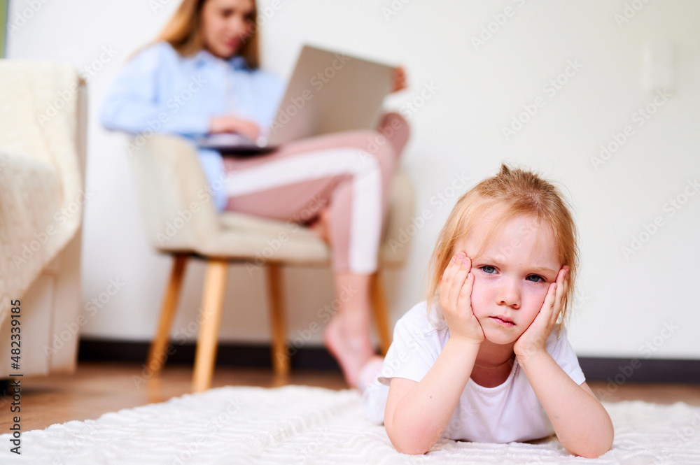 Upset little girl sitting lonesome while mother using laptop. Mother don't have time for daughter Upset little girl sitting lonesome while mother using laptop. Mother don't have time for daughter