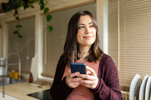 Contemplative woman with smart phone in kitchen at home