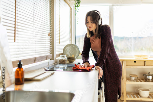 Woman listening music cleaning induction stove in kitchen at home photo