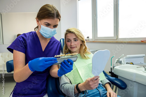  dentist woman in special clothes shows a palette of tooth colors for a female patient.