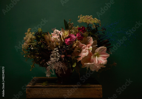 Modern and whimsical flower arrangement on a wooden box. Dark tone picture. Flowers in a spotlight. Horizontal dark green flower picture. photo