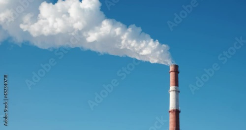 Red and white brick pipe of a thermal power station with white smoke. Production pipe with white smoke. Chimney on blue sky background. Concept of ecology, emissions, air pollution and atmosphere