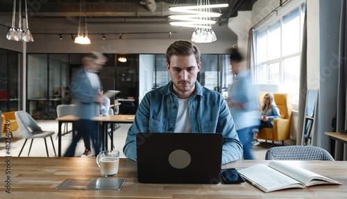 Fotografie Focused young freelance employee man working on project at laptop in office rush