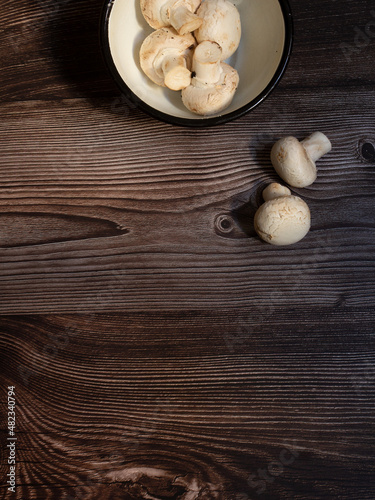 white rustic pewter bowl with raw mushrooms on dark wood