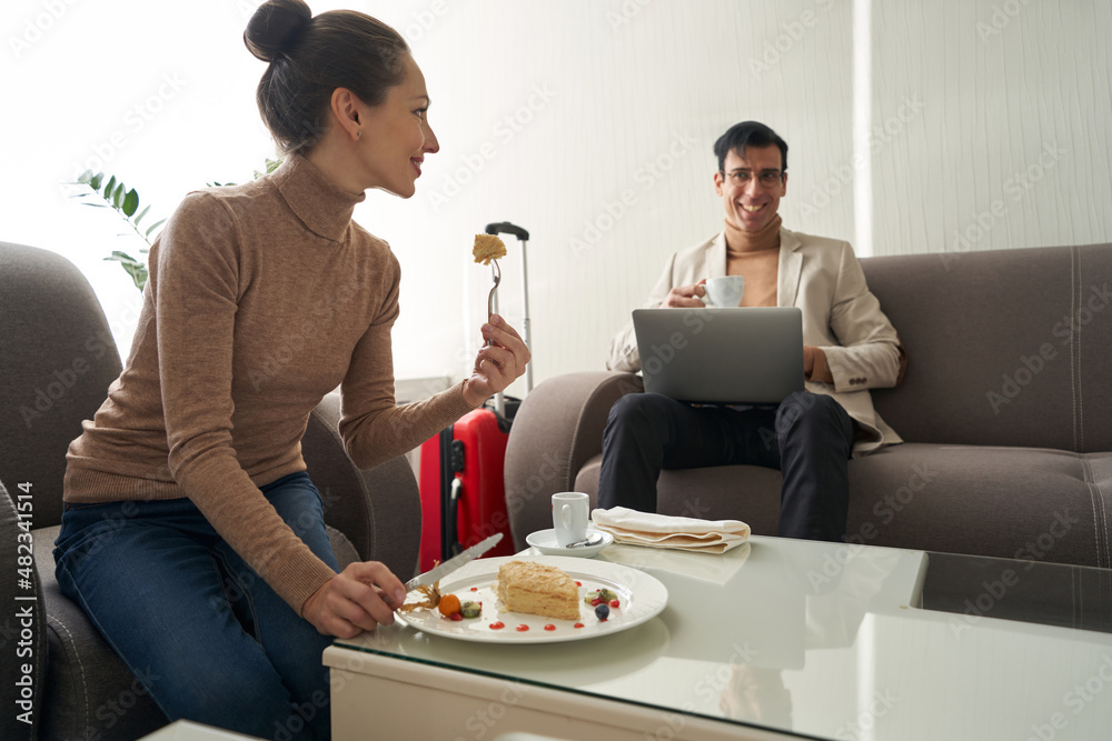 Woman eating cake and looking at man with laptop Woman eating cake and looking at man with laptop