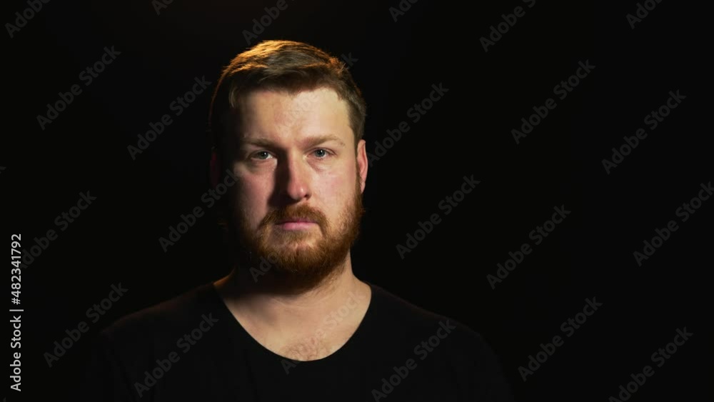 young European man with a red beard stands on a black background and looks into the frame emotion seriousness purposefulness severity young European man with a red beard stands on a black background and looks into the frame emotion seriousness purposefulness severity