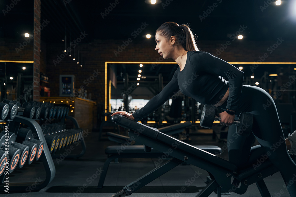 Fit young woman performing single-arm dumbbell exercise Fit young woman performing single-arm dumbbell exercise