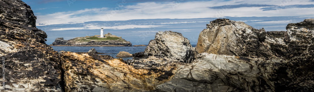 Panoramic view of a white lighthouse through a gap in the rocks.