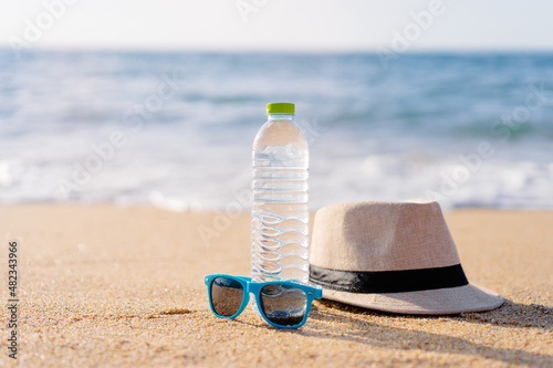 Vacation and protection. Essentials on the sea beach. Bottle of drinking water, sunglasses and hat.