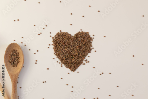 Heart made of raw lentils on a white background with kitchen utensils