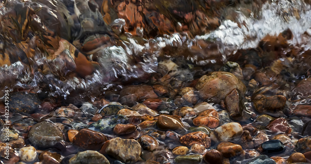Background with colorful round sea pebble stones and foam on the shore. Banner.
