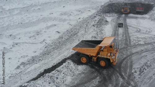 Large quarry dump trucks loaded with coal work at the coal mine in heavy snowfall.