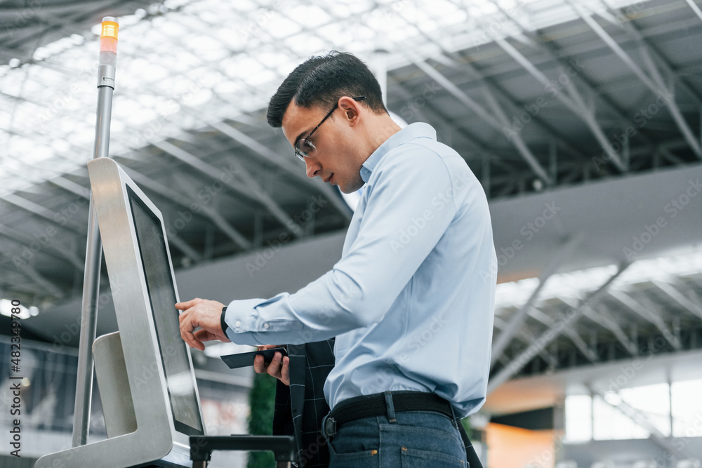 Standing by the terminal. Young businessman in formal clothes is in the airport at daytime Standing by the terminal. Young businessman in formal clothes is in the airport at daytime