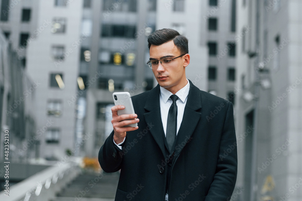 With smartphone. Businessman in black suit and tie is outdoors in the city With smartphone. Businessman in black suit and tie is outdoors in the city