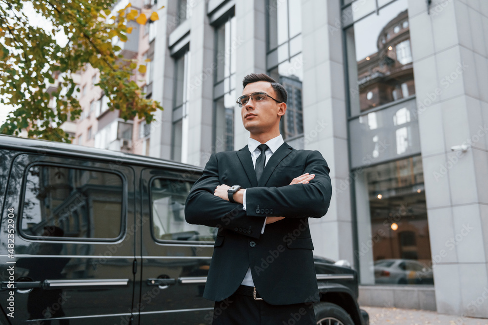 Standing with arms crossed. Businessman in black suit and tie is outdoors in the city Standing with arms crossed. Businessman in black suit and tie is outdoors in the city