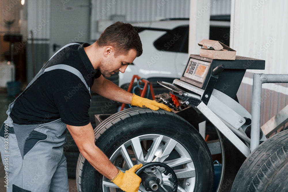 Taking the wheel. Man in uniform is working in the auto service Taking the wheel. Man in uniform is working in the auto service