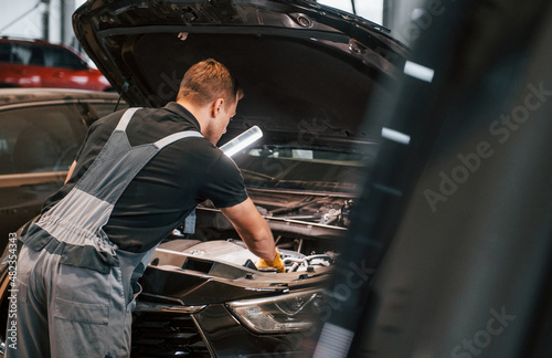 With lighting equipment. Man in uniform is working in the auto service