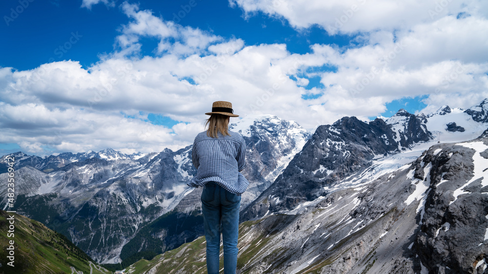 Girl traveler enjoys view summer alpine mountains and snow on slopes. Panoramic view of the over the alps. Italian mountains.