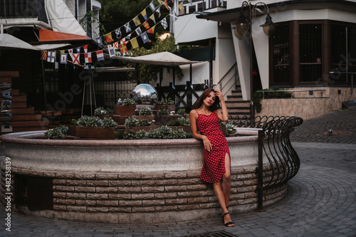 Beautiful sexy brunette girl in a red dress posing on the street with paving stones in Italy