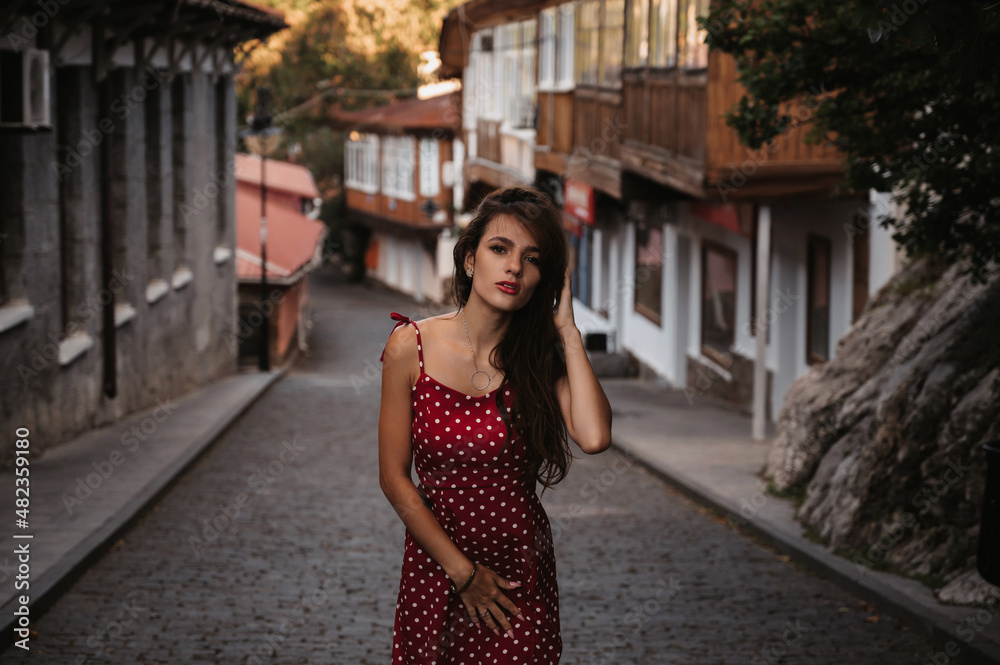 Naklejka premium Sexy young Caucasian girl in a red dress posing on a beautiful historical street in Europe
