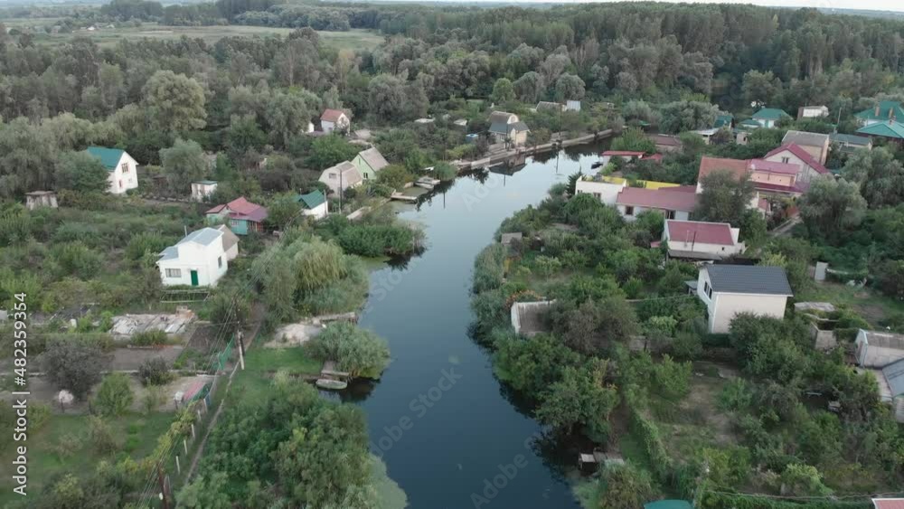 Flight over the little river on the banks of which there are houses. Around a lot of green trees in wetland Flight over the little river on the banks of which there are houses. Around a lot of green trees in wetland