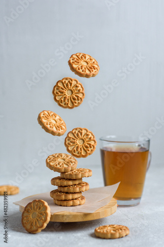 Levitation of cookies on a tray against a mug of tea and a light gray background