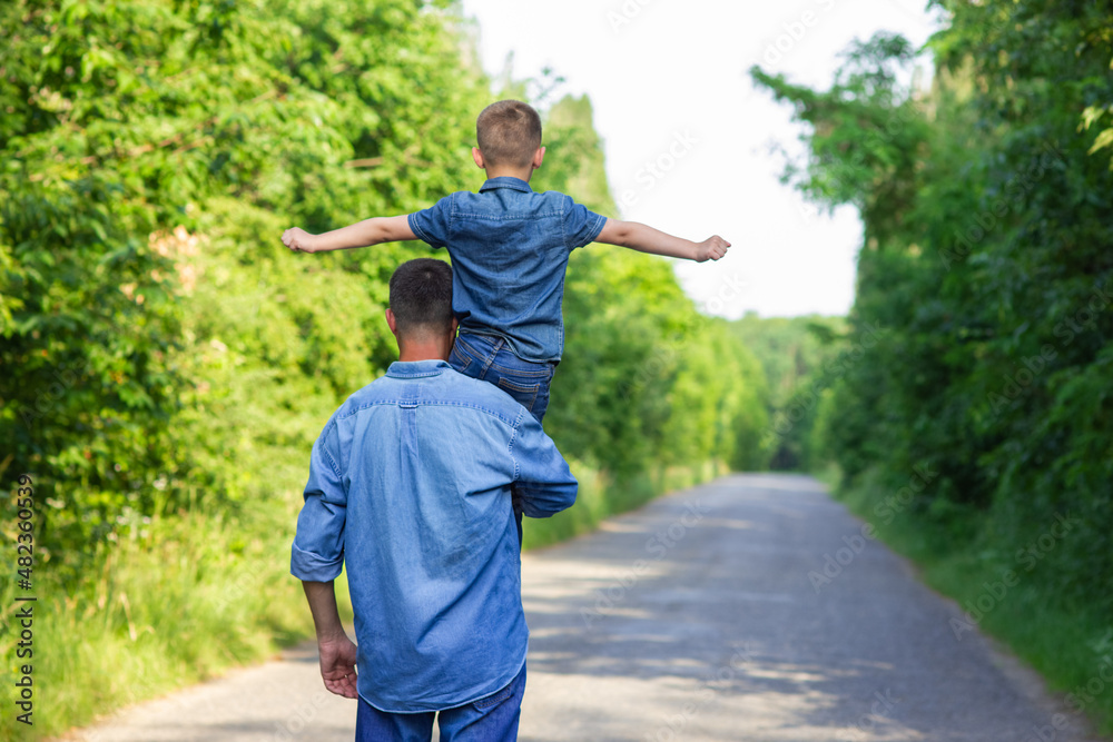 A Happy child with parent on shoulders walk along the road in park background