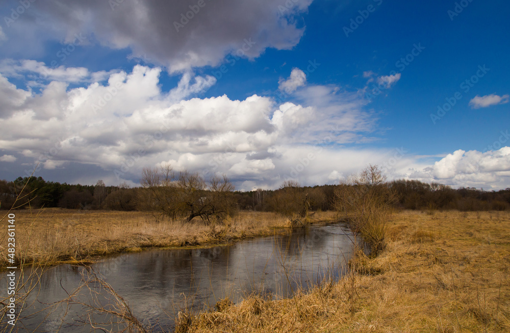 Spring in Belarus. Dry yellow grass, blue sky reflecting in the river. Warm pleasant april sunny day country side photo Spring in Belarus. Dry yellow grass, blue sky reflecting in the river. Warm pleasant april sunny day country side photo
