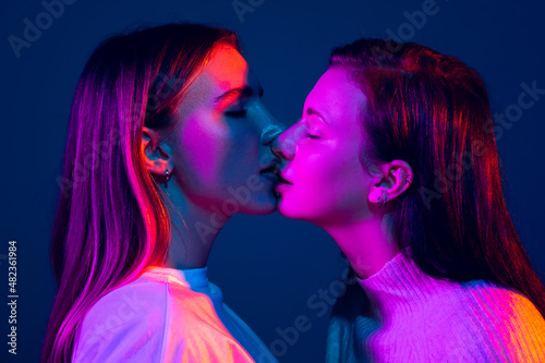 Close-up young girls, couple isolated on blue background in neon light. Concept of emotions, love, relations, romantic holidays.