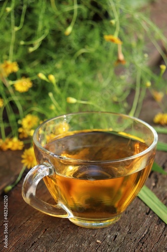 Hot tea on cup and yellow flower on wood background