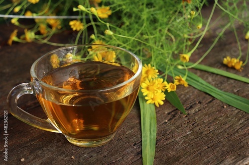 Hot tea on cup and yellow flower on wood background