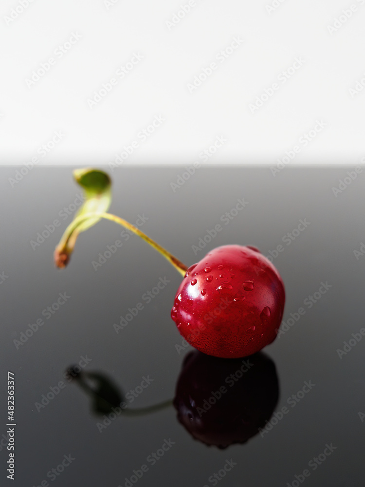 A single cherry and its reflection on dark surface A single cherry and its reflection on dark surface