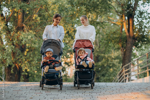 Two women friends walking with baby prams and their kids in park photo