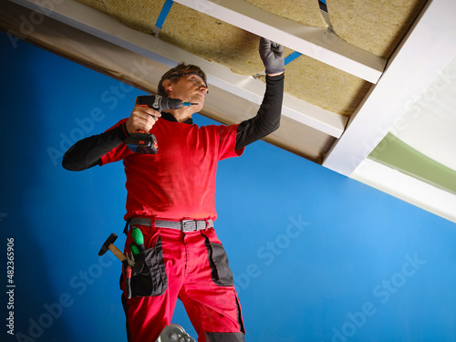 Rock wool applied to a wooden attic under renovation to save energy. Craftsman with work tools, applies rock wool panels in the attic.  photo