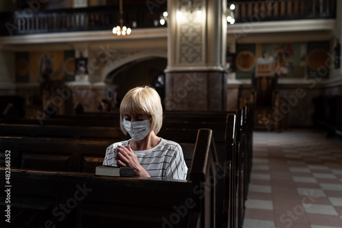 Masked woman is praying in the church. Religious concept, light of spiritual state. Close-up girl with bible © thomsond