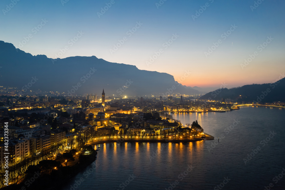 Lecco city on Lake Como aerial shot at sunrise with city lights.