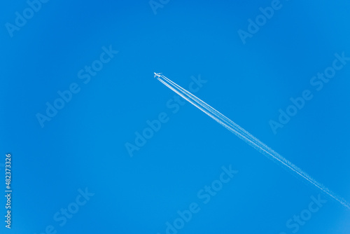 A white Airliner with contrails flying in a clear blue sky, seen directly below, photography.