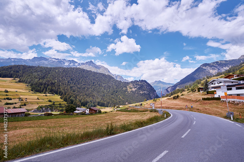 Asphalt road in Alps mountains at hills and mountain village background. Road trip concept.