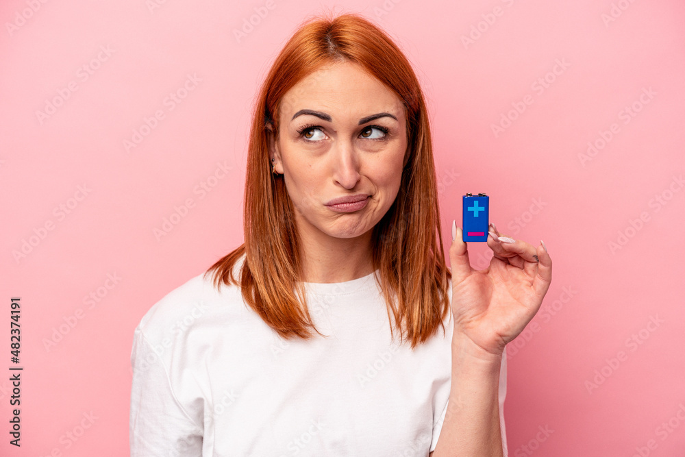 Young caucasian woman holding a batteries isolated on pink background confused, feels doubtful and unsure. Young caucasian woman holding a batteries isolated on pink background confused, feels doubtful and unsure.