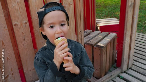 Beautiful boy caucasian preschool boy eating ice cream cone in Park .