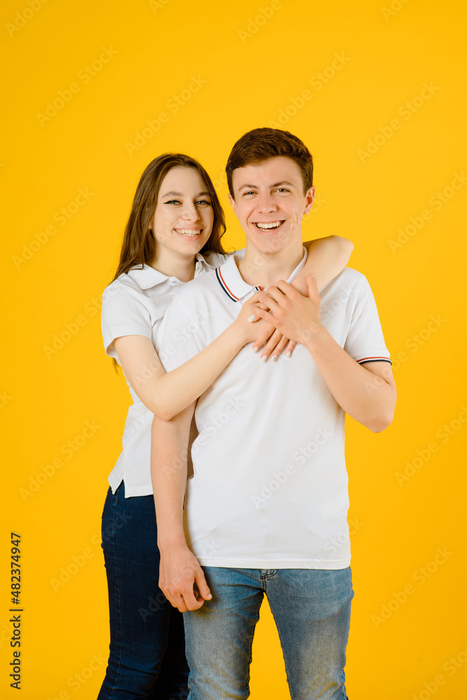 young happy couple man and woman in white t-shirts smiling and laughing on a yellow background.. young happy couple man and woman in white t-shirts smiling and laughing on a yellow background..