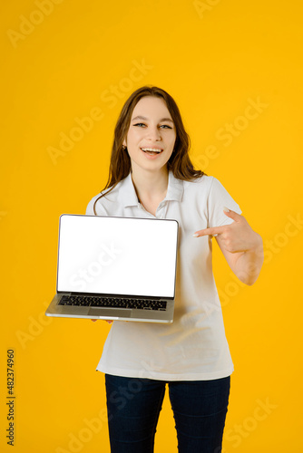 A Portrait of a young happy woman in white t-shirt smiling and holding a notebook computer on a yellow background.