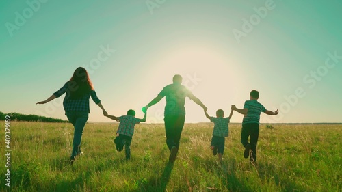 Happy family runs in park holding hands. Happy family walk silhouette of parents and children at sunset. Mom, dad sons walk together outdoors. Family holiday in nature, children's dreams and fantasies
