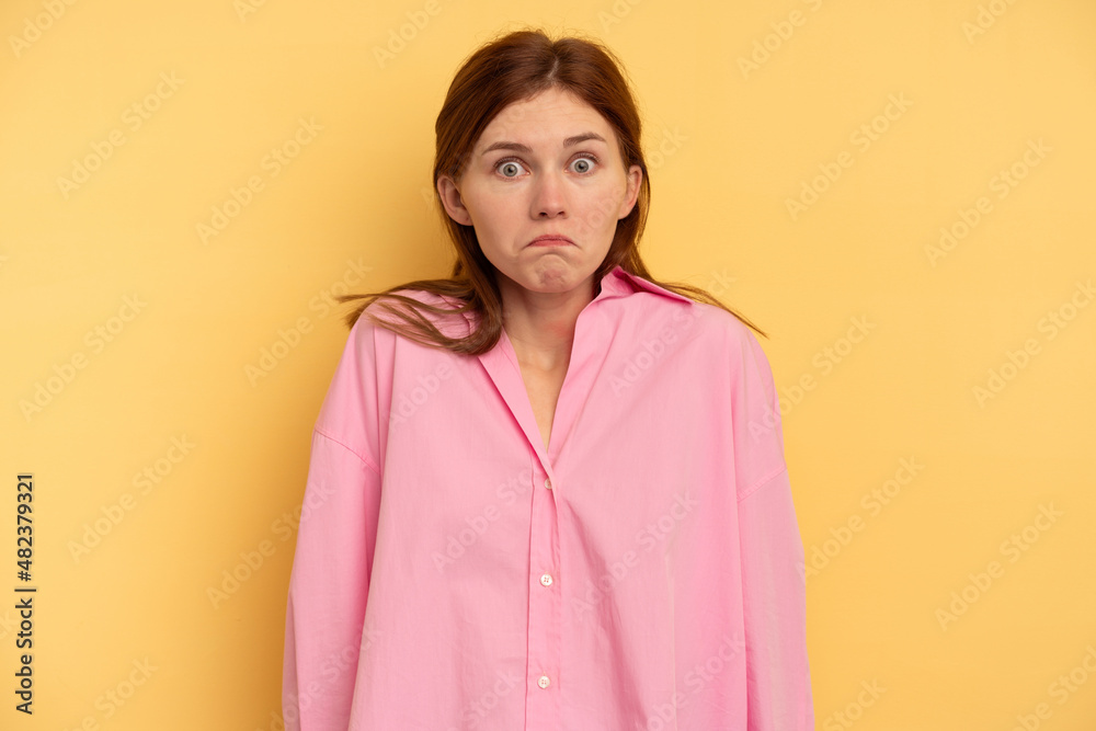 Fototapeta premium Young English woman isolated on yellow background shrugs shoulders and open eyes confused.