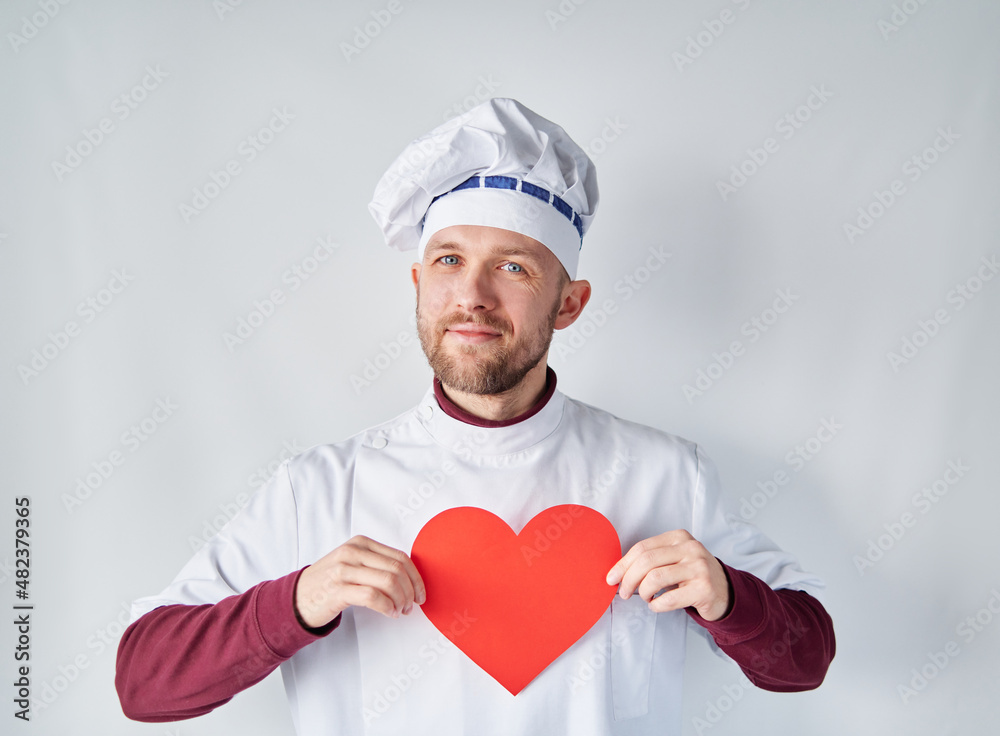 Attractive chef holding a red heart in front of the workwear. Bearded chef or baker man in white uniform with red paper heart shape as St. Valentine's day, romance or love concept. High quality photo Attractive chef holding a red heart in front of the workwear. Bearded chef or baker man in white uniform with red paper heart shape as St. Valentine's day, romance or love concept. High quality photo