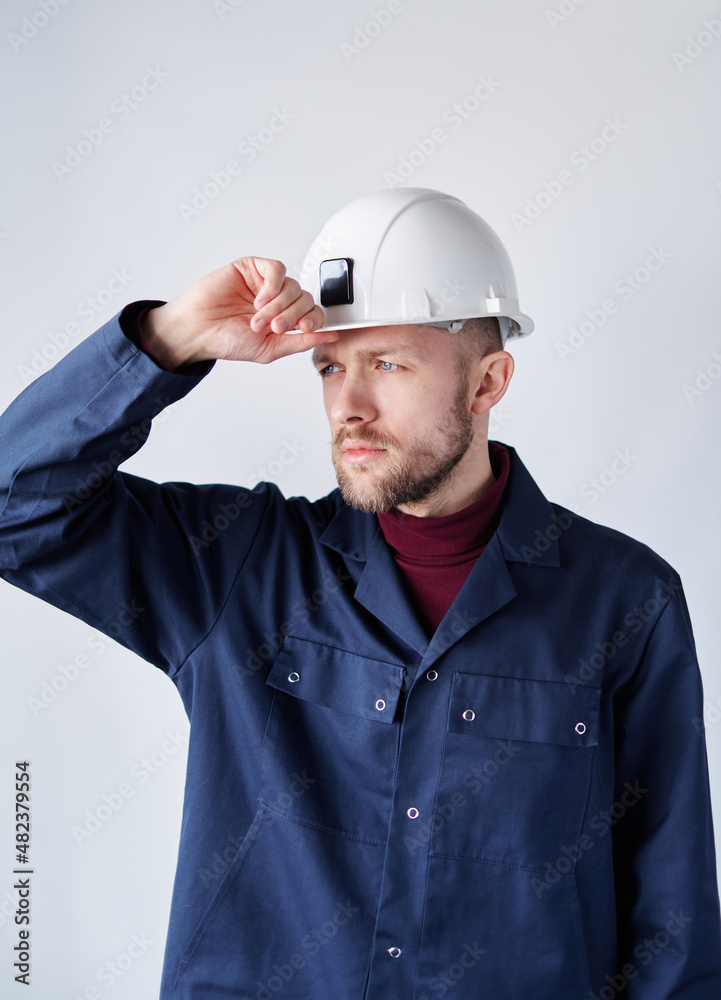 Building contractor, mechanic or electrician portrait. Serious cute caucasian bearded male supervisor, foreman or architect in uniform adjusting his hard hat. High quality vertical image Building contractor, mechanic or electrician portrait. Serious cute caucasian bearded male supervisor, foreman or architect in uniform adjusting his hard hat. High quality vertical image