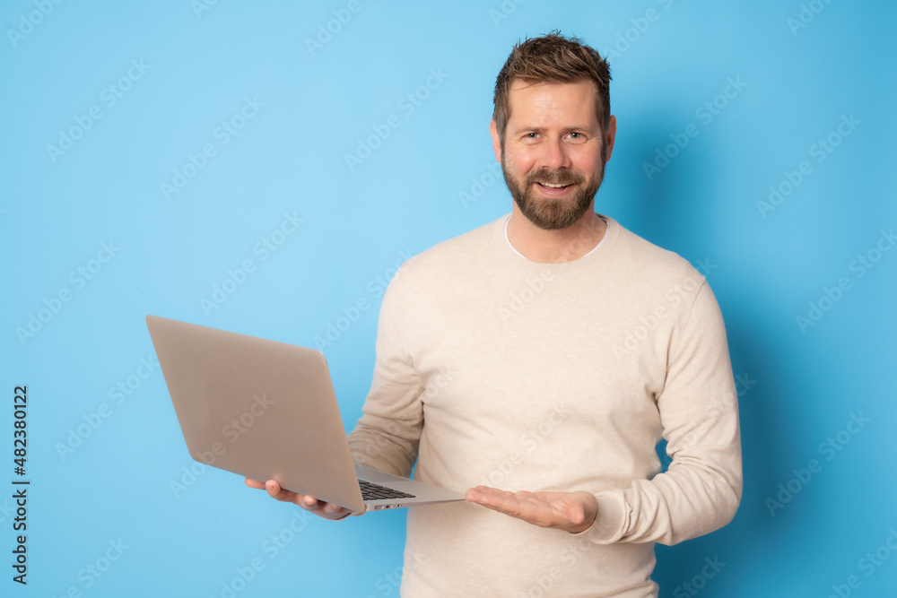 Young bearded man in casual clothing using laptop computer standing isolated over blue background. Young bearded man in casual clothing using laptop computer standing isolated over blue background.